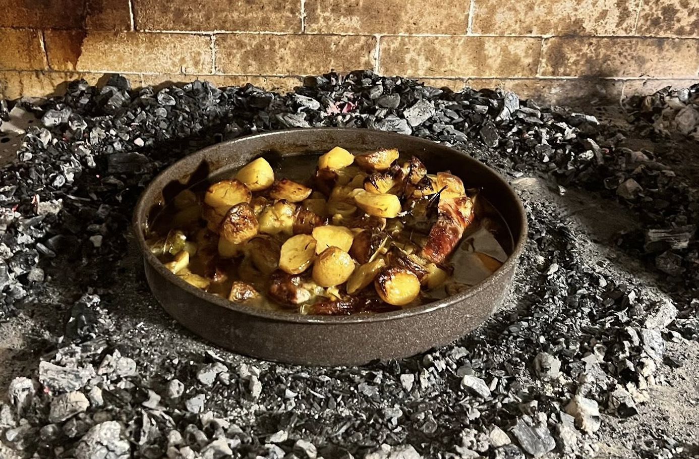 Peka roasting with potatoes in a pan over embers