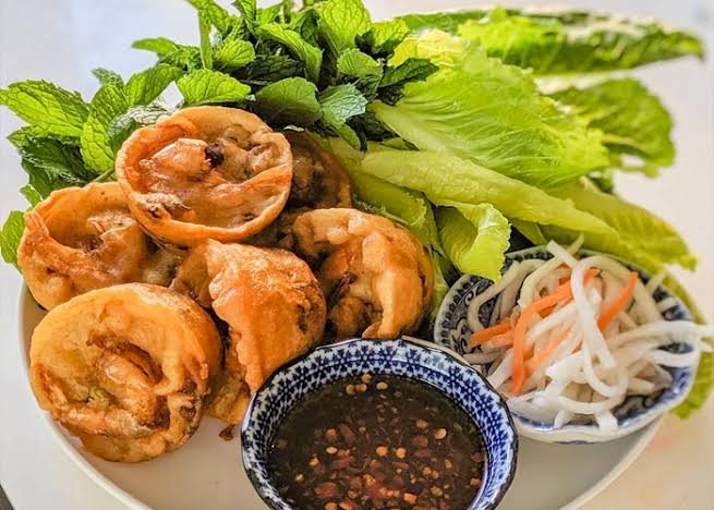 Plate of banh khot with herbs, lettuce, pickles, and dipping sauce