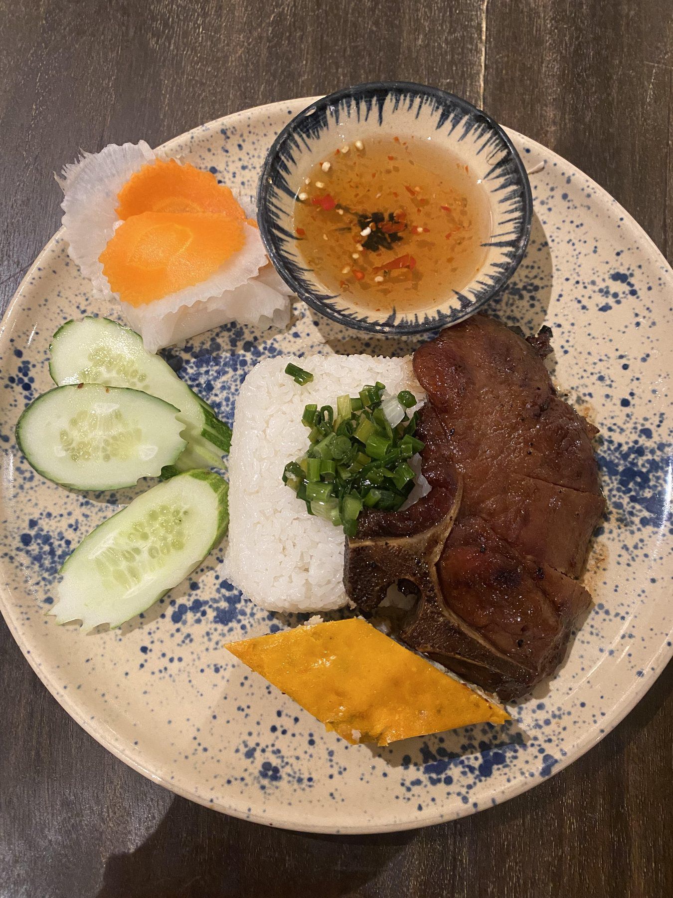 Plate of com tam with grilled pork chop, broken rice, pickles, cucumber, and fish sauce