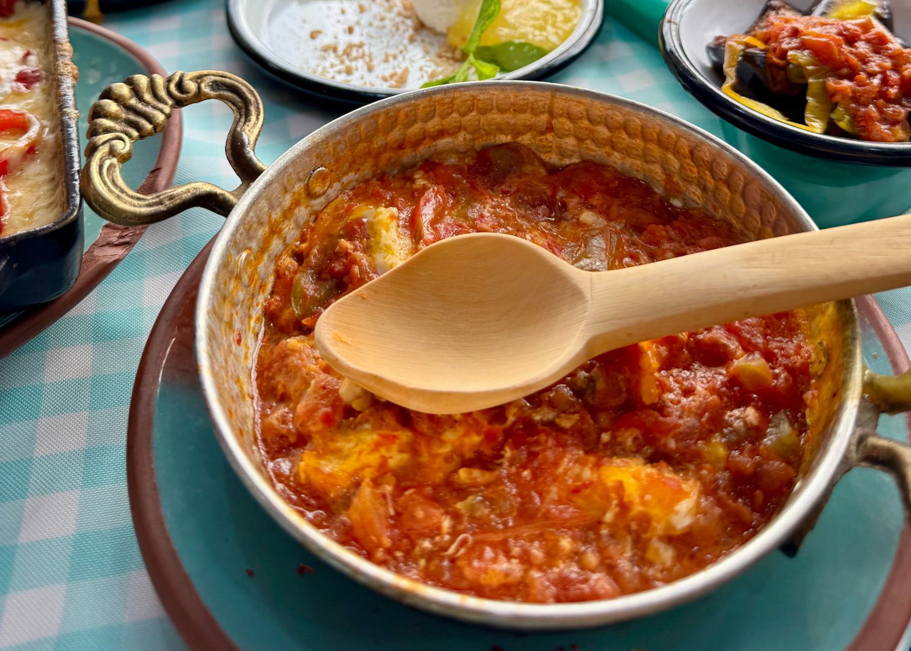 Menemen simmering in a copper pan with a wooden spoon