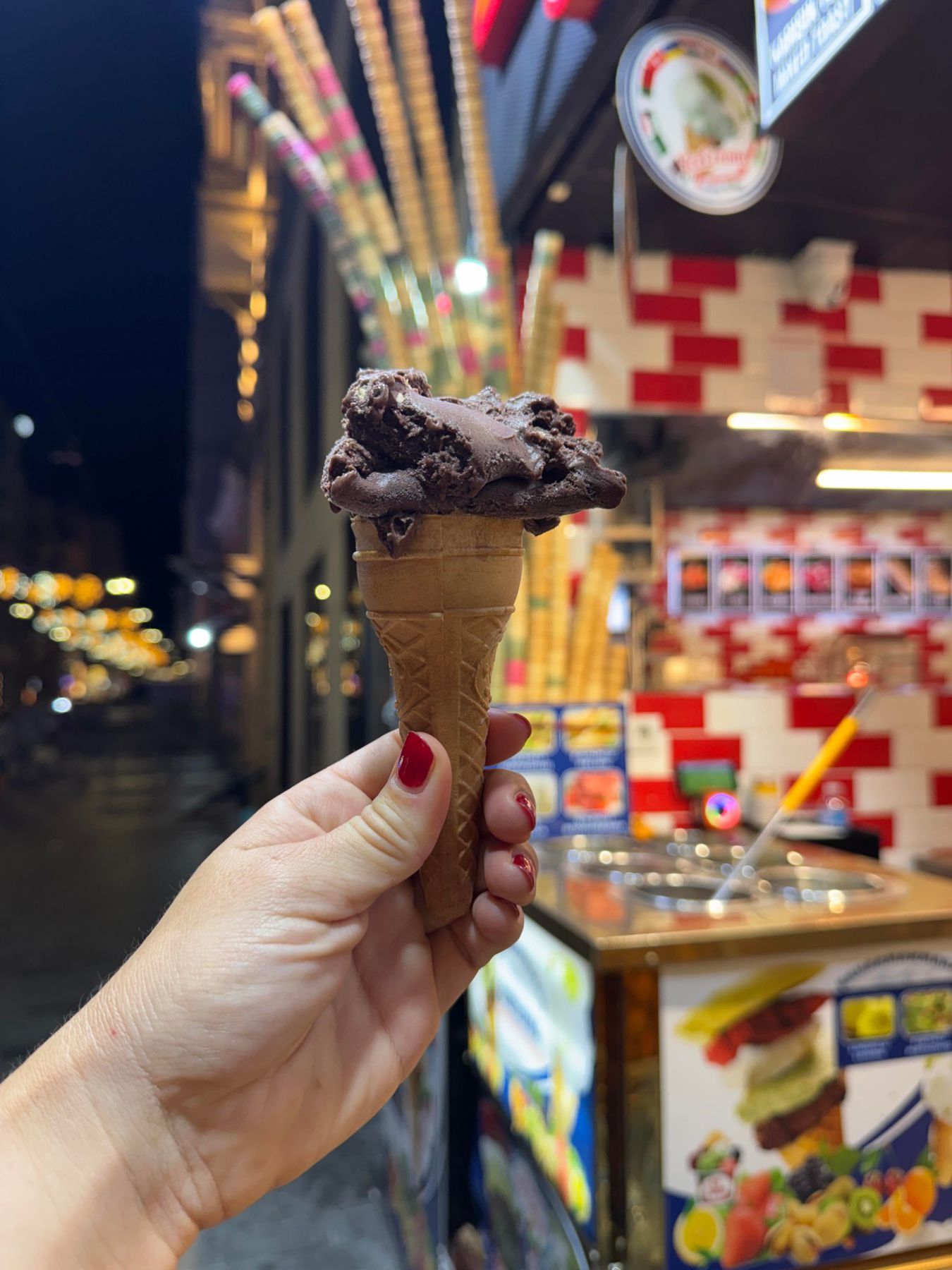 Hand holding a chocolate dondurma cone at an Istanbul ice cream stand at night