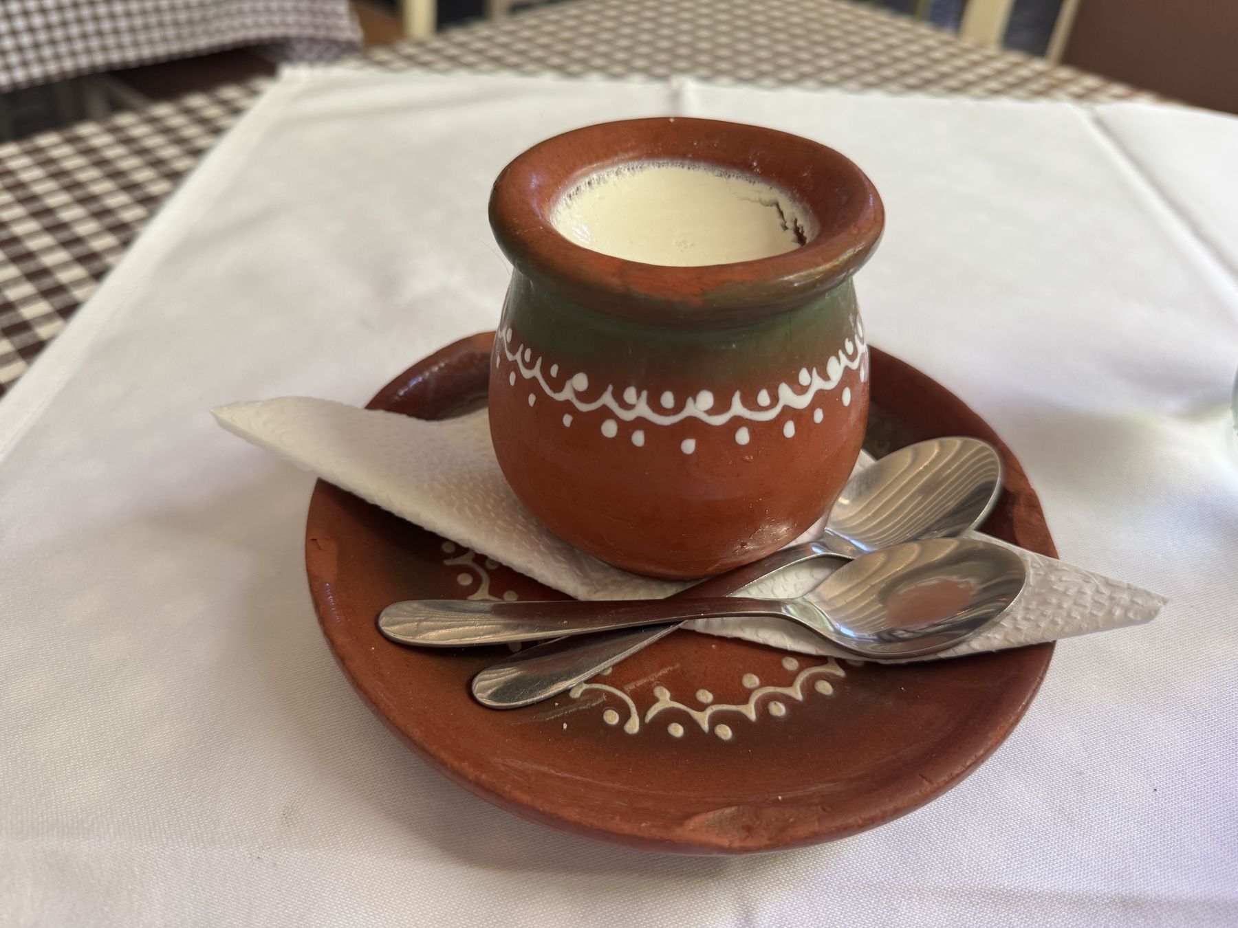 Clay pot of kiselo mleko served on a small plate with spoons