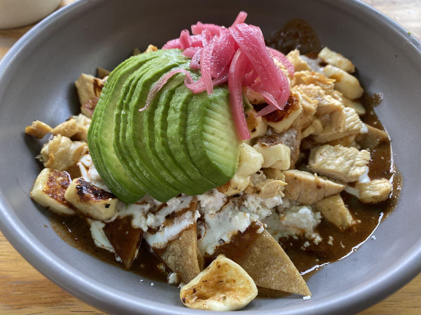 Bowl of chilaquiles topped with avocado, pickled onion, chicken, and cheese
