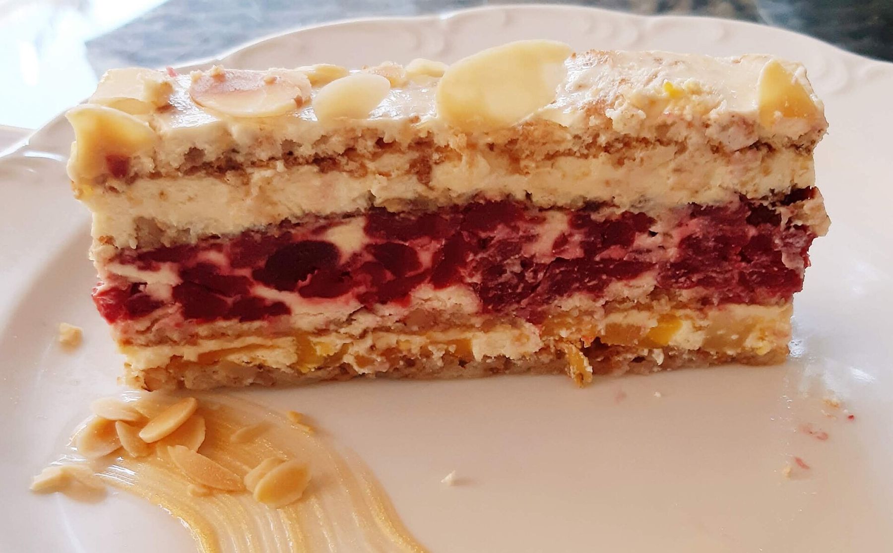 Slice of Moskva šnit layered with cream, fruit, and nuts on a white plate