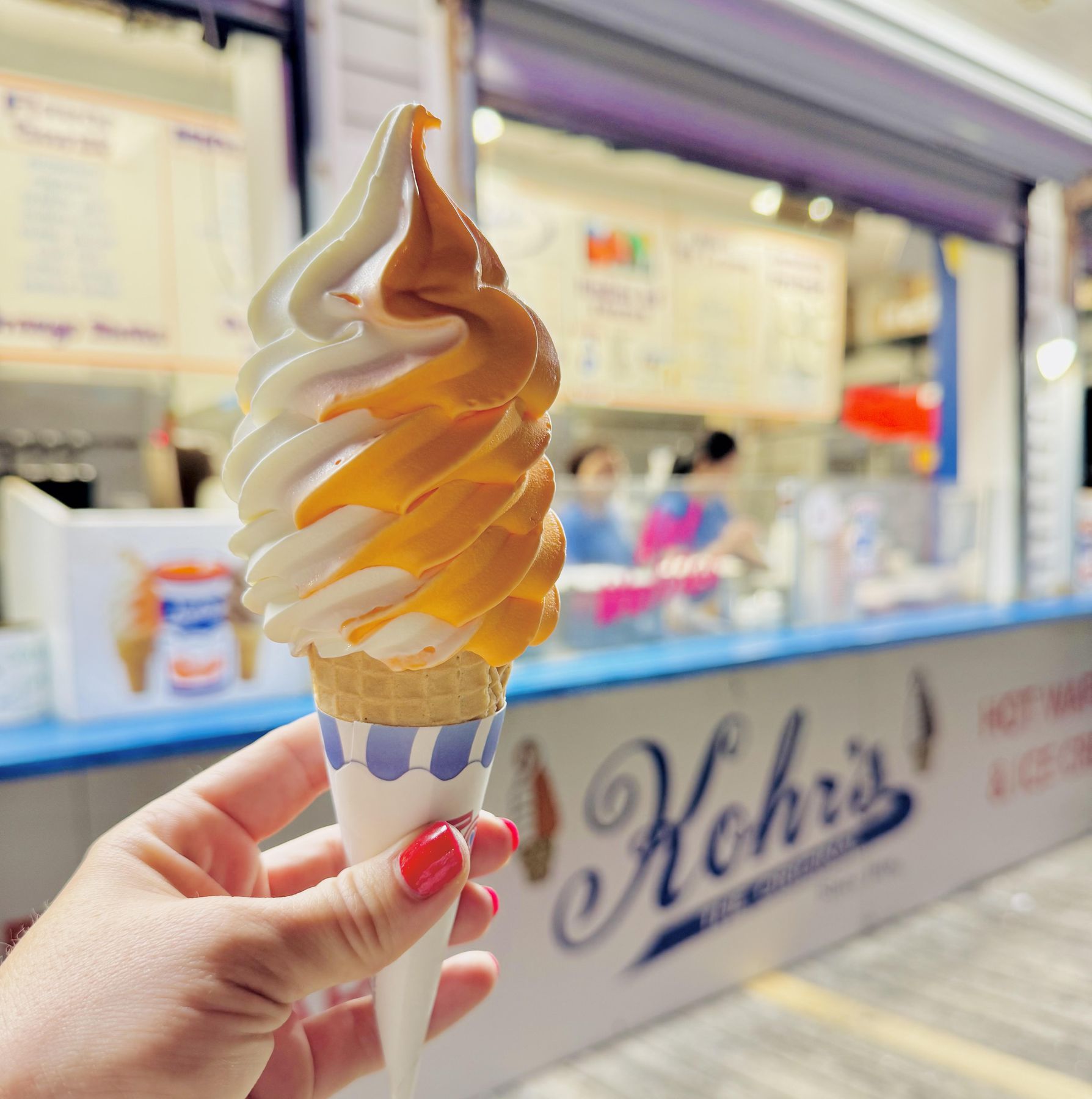 Orange and vanilla soft serve swirl in a cone held in front of a Kohr Bros. stand at the Jersey Shore