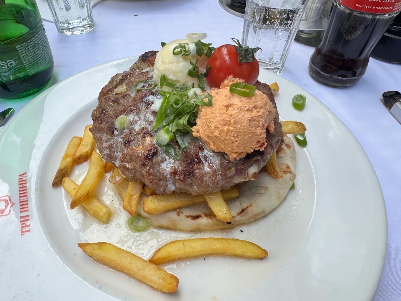Pljeskavica served on flatbread with fries, kajmak, and a spicy spread